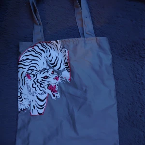 Tygväska med målat tigertryck - Handgjord grå tygväska med ett målat tryck av en vit tiger. Inte alls använd, den är i toppen skick.