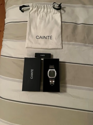 Grön och silver CAINTÈ klocka - Snygg klocka från CAINTÈ med grön urtavla och rutigt mönster. Klockan har en stilren silverfärgad länk i metall och en fyrkantig boett. Levereras i originalförpackning med tygpåse och box. Perfekt accessoar för dig som gillar modern design.