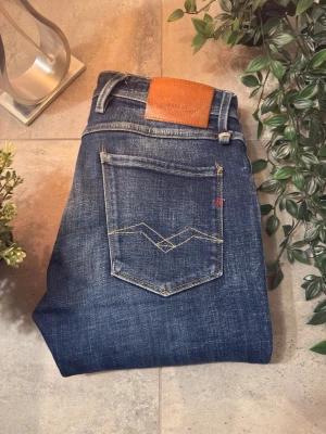 Blå Replay jeans - Snygga Replay Anbass jeans i mörkblå tvätt med klassiska detaljer och kontrastsömmar. Replay-logga på bakfickan och läderpatch i midjan. Perfekt för dig som gillar stilrena och moderna jeans. Skriv för funderingar!