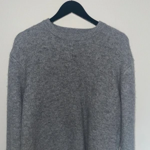 Grå stickad tröja med rund hals - Mysig grå stickad tröja med rund hals och långa ärmar. Perfekt för kyliga dagar och enkel att matcha med jeans eller kjol. Tröjan har en klassisk och avslappnad passform som gör den superbekväm att bära.