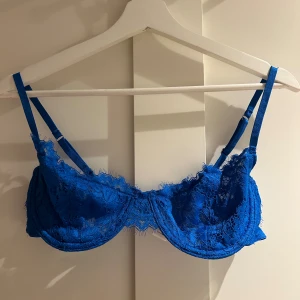 Blå spetsig BH från Bik Bok - Säljer en blå bh från Bik Bok i storlek L. Den har tunna justerbara axelband och är gjord i genomskinlig spets med fina detaljer. Perfekt för dig som vill ha något snyggt och edgy i garderoben.