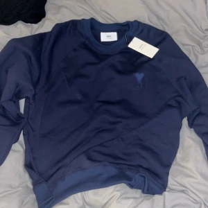 Mörkblå sweatshirt från Ami Paris - Säljer en mörkblå sweatshirt från Ami Paris med broderad logga på bröstet. Tröjan har rund halsringning, långa ärmar och är gjord i mjuk bomull. Perfekt för dig som gillar stilrena och trendiga plagg.