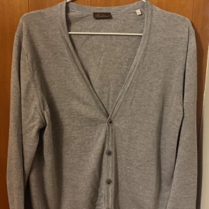 Grå kofta från Stenströms, M - Snygg grå kofta från Stenströms i storlek M. Koftan har v-ringning, 6 knappar framtill och är tillverkad i mjukt merino ull. Perfekt för lager-på-lager och enkel att matcha med olika outfits.