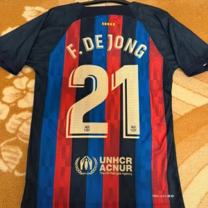 FC Barcelona F. De Jong matchtröja Nike - Säljer en officiell FC Barcelona fotbollströja med F. De Jong och nummer 21 på ryggen. Tröjan är kortärmad, har klassiska blå och röda ränder, klubbmärke, Nike-logga och Spotify som sponsor. Tillverkad i lätt funktionsmaterial för bästa komfort.