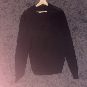 Svart stickad tröja från J.Lindeberg - Svart stickad tröja från J.Lindeberg med diskret logga på bröstet. Tröjan har lång ärm, ribbade muddar och dragkedja vid halsen. Snygg och stilren modell som passar perfekt till kyliga dagar. Endast använd 1 gång jättefint skick. Ny pris 1500