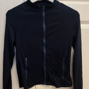 Mörkblå träningströja med dragkedja - Mörkblå träningströja med hel dragkedja framtill och två ficko. Jackan har en enkel, sportig design och är långärmad. Perfekt för dig som gillar en clean och stilren look.