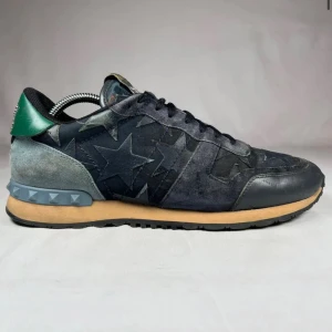 Valentino Garavani Rockrunner sneakers - Snygga Valentino Garavani Rockrunner sneakers i mörkblå mocka och skinn med stjärnmönster. Skorna har svarta snören, grön detalj på hälen och en beige sula med nitar på bakkappan. Perfekt för dig som vill sticka ut med exklusiva och unika sneakers. Skorna levereras utan dustbagen och utan boxen. Priset går absolut att diskutera! //By, Olsén, Closet.