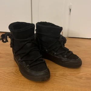 Svarta Inuikii boots med snörning - Svarta boots från Inuikii med grov snörning runt hela skon och mjukt foder på insidan. Skorna har en platt sula och är tillverkade i mocka och skinn, perfekta för kyliga dagar. Klassisk rund tå och robust design. Köptes på SELLPY jag har inte använt dom men köptes med bra skick så därför ja går ner hälften av priset!😊