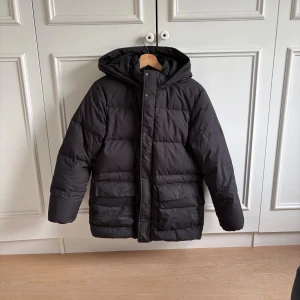 Svart pufferjacka från Uniqlo - Svart pufferjacka från Uniqlo med huva och stora fickor framtill. det är storlek 13 år men den passar även som Xs då den är lite oversized