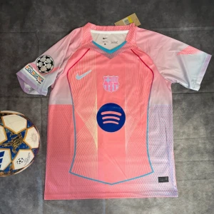 Barça Lamine Yamal 10 rosa Nike tröja - Snygg FC Barcelona fotbollströja i rosa och ljuslila med Lamine Yamal 10 på ryggen. Nike Dri-FIT material, kortärmad modell med blå detaljer och tryckta loggor från Spotify och UEFA Foundation. Perfekt för dig som vill sticka ut på planen eller läktaren.