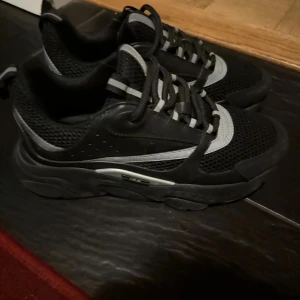 Svarta chunky sneakers med meshdetaljer - Säljer ett par svarta chunky sneakers med silvriga och grå detaljer. Skorna har en tjock sula, meshpartier för extra andningsförmåga och snörning framtill. Perfekta för dig som gillar sportig och modern stil.