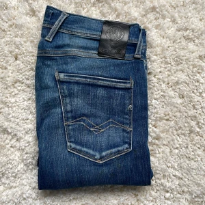Replay Anbass jeans  - Snygga blå jeans från Replay, modell Anbass. De har klassisk femficksdesign, smal passform och tydliga slitningar för en cool look. Jeansen är tillverkade i stretchigt denim för extra komfort och har Replay-logga på bakfickan och läderpatch i midjan.