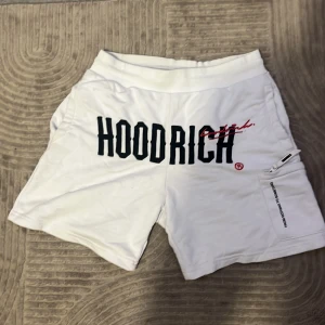 Vita Hoodrich shorts med tryck XS - Säljer ett par vita shorts från Hoodrich i storlek XS. De har stor svart och röd logotyp framtill, textdetaljer bak och en ficka med dragkedja på sidan. Fick dessa för 1 år sen och använde dom ett bra tag. Inga synliga skador eller fläckar på shortsen. 