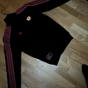 Manchester United x Adidas svart ziptröja helt ny  - Svart ziptröja från Adidas x Manchester United med röda och vita ränder längs ärmarna, broderad klubbmärke på bröstet och Adidas-logga. Hög krage, långärmad och med dragkedja framtill. Perfekt för fotbollsfans som vill sticka ut. Riktigt fin tröja som är HELT NY köpt för 1800 på stadium men säljes för 1000kr eller byta mot en annan  st S men passar medium oxå 