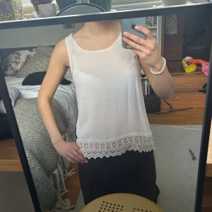 Vit linnetopp med spetskant - Säljer en ljusvit linnetopp med rund halsringning och ärmlös design. Toppen har en snygg spetskant längst ner som ger en extra detalj. Materialet är lätt och luftigt, perfekt för varma dagar. Enkel och stilren look som funkar till många outfits.