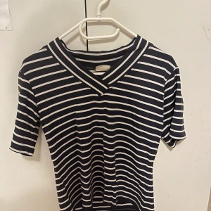 Randig t-shirt från Kellermann - Mörkblå och vit randig t-shirt från Kellermann Scandinavia i storlek M. T-shirten har v-ringning och korta ärmar. Perfekt för en avslappnad och stilren look. Materialet känns mjukt och bekvämt mot huden.