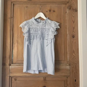 Ljusblå blus med spets från Lindex - Supersöt ljusblå blus från Holly & Whyte by Lindex. Blusen har volangärmar, spetsdetaljer och en liten krage. Materialet är mjukt och luftigt bomull, perfekt för vår och sommar. Snyggt mönstrad och gulliga detaljer.