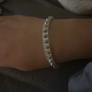 Silvrigt armband med nitar - Snyggt armband i silverfärg med coola nitdetaljer runt hela bandet. Perfekt för dig som gillar en edgy stil och vill ha något som sticker ut på handleden. Armbandet har en enkel och stilren form som passar till många outfits.