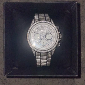 Glittrig silverklocka från Dissing - Säljer en riktigt blingad klocka från Dissing i silverfärg med massor av gnistrande stenar på både urtavla och armband. Klockan har rund form, kronograf och länkarmband. Extra länkar medföljer så du kan anpassa storleken. Perfekt för dig som gillar att sticka ut. Kvitto finns! 