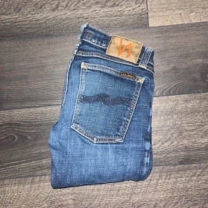 Nudie jeans  - Säljer ett par klassiska blå jeans från Nudie Jeans med snygga slitningar och kontrastsömmar. Jeansen har fem fickor. Modell Long John. Midja 31cm, längd 91cm. Ifall det inte finns någon bild i annonsen där jag bär plagget så är det för att jag ej kan ha storleken heller passformen, så kolla måtten för storlek och googla på modellnamnet för passform 😉S3