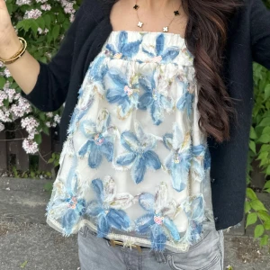 Blommig linnetopp XS - Supersöt linnetopp från SHEIN i storlek XS. Toppen är vit med stora blå 3D-blommor och små paljettdetaljer. Den har tunna axelband och en luftig, croppad passform. Perfekt för sommarens alla tillfällen när du vill sticka ut lite extra.