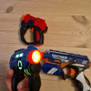 Hot Fire & LED Laser Toy Guns - Säljer ett paket med tre leksakspistoler: två LED-laserpistoler med ljus och ljud samt en Hot Fire dartpistol. Alla i fint skick, inga synliga skador eller slitage. Perfekt för lek och spel inomhus eller utomhus. Batteridrivna laserpistoler med coola ljuseffekter.