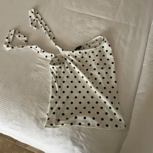 Prickig vit oneshoulder topp från Amisu - Supersöt vit topp med svarta prickar från Amisu. Modellen är oneshoulder med en bred axelrem som kan knytas. Sitter snyggt och har en slim passform. Perfekt för dig som gillar att sticka ut med ett lekfullt mönster. Materialet är mjukt och stretchigt, troligen polyester.