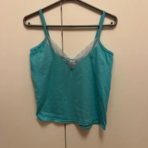 Turkos linnetopp med spets från H&M strl L / 42-44 - Turkos linnetopp från H&M i storlek L / 42-44, tillverkad i 100% bomull. Toppen har smala axelband och en snygg v-ringning med ljus spetsdetalj framtill.