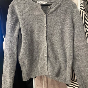 Grå kofta från ZARA med knappar - Mysig grå kofta från ZARA i storlek L. Koftan är stickad och har långa ärmar samt silverfärgade knappar framtill. Perfekt att slänga på sig när det är kyligt ute.