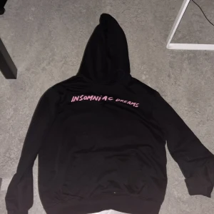 Svart hoodie Insomniac Dreams H&M - Svart hoodie från H&M med coolt rosa tryck 'INSOMNIAC DREAMS' fram och bak, samt grafiskt motiv på ryggen. Tröjan har huva med snörning och en stor magficka. Materialet är mjuk bomull och polyester, perfekt för chill dagar.