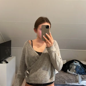 Grå omlottkofta från Kappahl - Supermysig grå omlottkofta från Kappahl med knyt i sidan. Koftan är stickad, har v-ringning och långa ärmar. Perfekt för lager-på-lager och chill dagar. Snygg och enkel att matcha med jeans eller kjol.