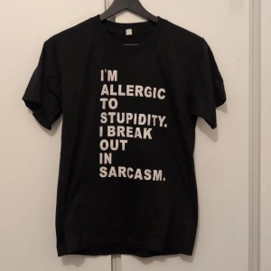 Svart t-shirt med sarkastiskt tryck - Svart t-shirt med vit text framtill: 'I'M ALLERGIC TO STUPIDITY. I BREAK OUT IN SARCASM.' Klassisk rund hals och korta ärmar. Materialet känns som mjuk bomull, perfekt för dig som gillar att sticka ut med humor.