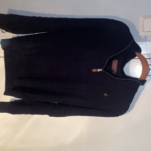 Marinblå stickad half zip-tröja Morris - Säljer en marinblå stickad tröja från Morris med half zip och kabelstickat mönster. Tröjan har långärmade och ribbade muddar samt en liten Morris-logga broderad på bröstet. Perfekt för dig som gillar klassisk stil och snygga detaljer. Fint skick. Passar 160-170cm. OBS Den har krympt i tvätten därför står det L på lappen!  