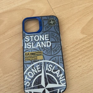 Stone Island skal - Snyggt Stone Island-skal för iPhone med unikt tryck och blå ram runt kamran. Skalet är i ny skick . Perfekt för dig som vill skydda din mobil och samtidigt sticka ut med en stilren design. Passar till iPhone 13 och 14