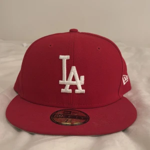 Röd LA Dodgers keps från New Era - Snygg röd 59FIFTY keps från New Era med LA Dodgers broderat i vitt framtill och New Era-logga på sidan. Platt skärm i rött med grå undersida. Klassisk baseballstil.