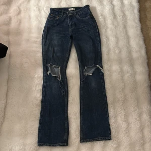 Blå bootcut jeans från Gina Tricot - Snygga blå jeans från Gina Tricot med bootcut passform och slitna hål på båda knäna. Jeansen har en mörk tvätt och är tillverkade i jeansmaterial. Pris kan diskuteras 