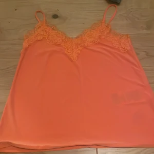 Orange linnetopp med spets från Amisu - Säljer en orange linnetopp från Amisu i storlek XS. Toppen har tunna axelband och v-ringning med fina spetsdetaljer framtill. Perfekt för varma dagar eller som ett lager under en kavaj. Har aldrig kommit till användning.🥰