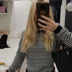 Svartvit mönstrad tröja CorteFiel - Snygg mörkblå/svart vit stickad tröja från CorteFiel med coolt rutigt mönster. Rund halsringning och svarta muddar vid ärmslut och nederkant. Perfekt till jeans och har en normal passform med långa ärmar. Materialet är mjukt och känns skönt mot huden.