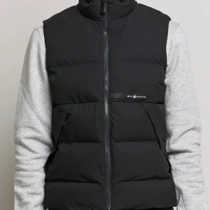 Äkta Sail Racing Race T8 Vest  - Slutsåld svart dunväst från Sail Racing med hög krage och dragkedja framtill i storlek M. Västen har två snedställda fickor och diskret logga på bröstet. Yttermaterialet är slätt och insidan är fodrad i blankt tyg. Perfekt för lager-på-lager under kyliga dagar. Västen är som ny köpt för 3000kr använd 2 gånger.
