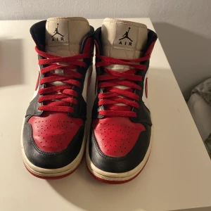 Nike Air Jordan 1 High röd/svart/vit - Nike Air Jordan 1 High sneakers i klassisk röd, svart och vit färg. Skorna har snörning med röda skosnören, rund tå och platt sula. Ikonisk Jumpman-logga på tungan och Air Jordan Wings på sidan. Tillverkade i skinn med perforerad tå för extra ventilation.