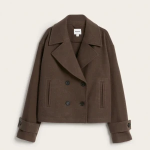 Brun skepparkavaj från Kappahl - Stilren brun skepparkavaj från Kappahl med dubbelknäppning och bred krage. Jackan har långa ärmar med knappar vid ärmslut och raka fickor framtill. Perfekt för dig som gillar klassisk och tidlös stil.