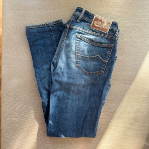  Jacob Cohen jeans  - Snygga blå jeans från Jacob Cohen med slitningar och hål på knäna för en cool, avslappnad look. Klassisk femficksmodell med ljus tvätt och kontrastsömmar. Jeansen har normal passform och är tillverkade i mjukt bomullstyg. Storleken är W34 men passar dig som har 32