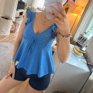 Blå broderad linnetopp med volang - Supersöt blå linnetopp med broderade detaljer och volangärmar. Perfekt för varma dagar…och perfekt med ett par gulliga shorts😉