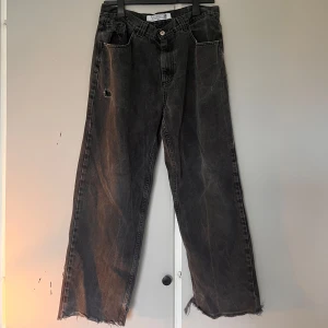 Svarta wide jeans från Polar 93Denim - Säljer ett par svarta jeans från Polar 93Denim med bred passform och råa, fransiga benslut. Jeansen har slitna detaljer och hål vid fickan för en riktigt edgy look. Hög midja och klassisk femficksdesign. Perfekta för dig som gillar streetstyle.