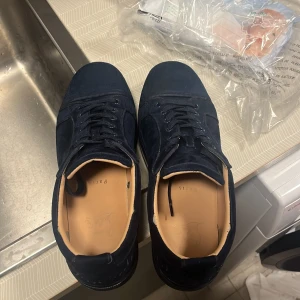 Mörkblå sneakers från Christian Louboutin - Säljer ett par mörkblå sneakers från Christian Louboutin i mocka med klassisk röd sula. Skorna har rund tå, snörning och en stilren design. Perfekta för dig som vill ha något exklusivt och snyggt till din outfit. Köpta för 3599 säljer för 1900, allt finns😃