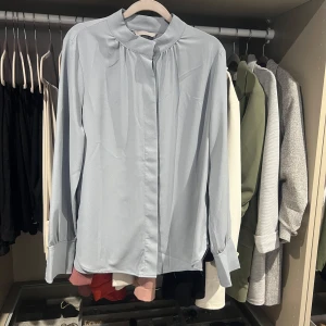 Ljusblå blus med ståkrage - Snygg ljusblå blus med lång ärm och ståkrage. Den har dolda knappar framtill och breda manschetter med knappar. Materialet känns mjukt och har ett lätt fall. Storlek S/XS