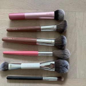 Set med sminkborstar från CAIA & RT - Säljer ett set med sex sminkborstar: fyra från CAIA (modeller F05, F06, F17, F19 i rosa, vit och nude),  en från Real Techniques i metallicrosa (modell 449) och en svart ögonskuggsborste av okänt märke.