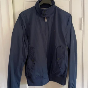 Marinblå windbreaker från J.Lindeberg - Snygg marinblå windbreaker (vindjacka) från J.Lindeberg med hög krage, dragkedja och knappar framtill. Jackan har två fickor med lock och knapp. Säljer för 599 (förhandlingsbart vid snabb affär!) storlek: M. Tveka inte att höra av er med funderingar!
