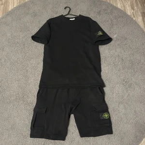 Svart Stone Island set - Svart t-shirt från Stone Island med klassisk rund hals och ikonisk logotyp-patch på vänster ärm. Med samma stil på shortsen. Strl M