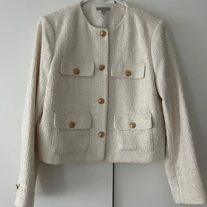 Beige kavaj i bouclé från H&M, stl 44 - Stilren beige kavaj från H&M i bouclé-liknande tyg med fyra fickor framtill och snygga guldknappar. Rak passform, rund halsringning och helfodrad insida. Perfekt för dig som gillar klassisk och trendig look. Den är i storlek 44 men är liten i storleken, är i typ s/m! Pris 300kr,ordinarie 599kr